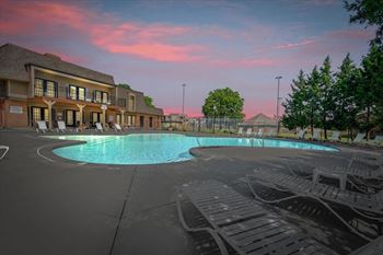 A large outdoor swimming pool surrounded by lounge chairs and a building with a balcony.